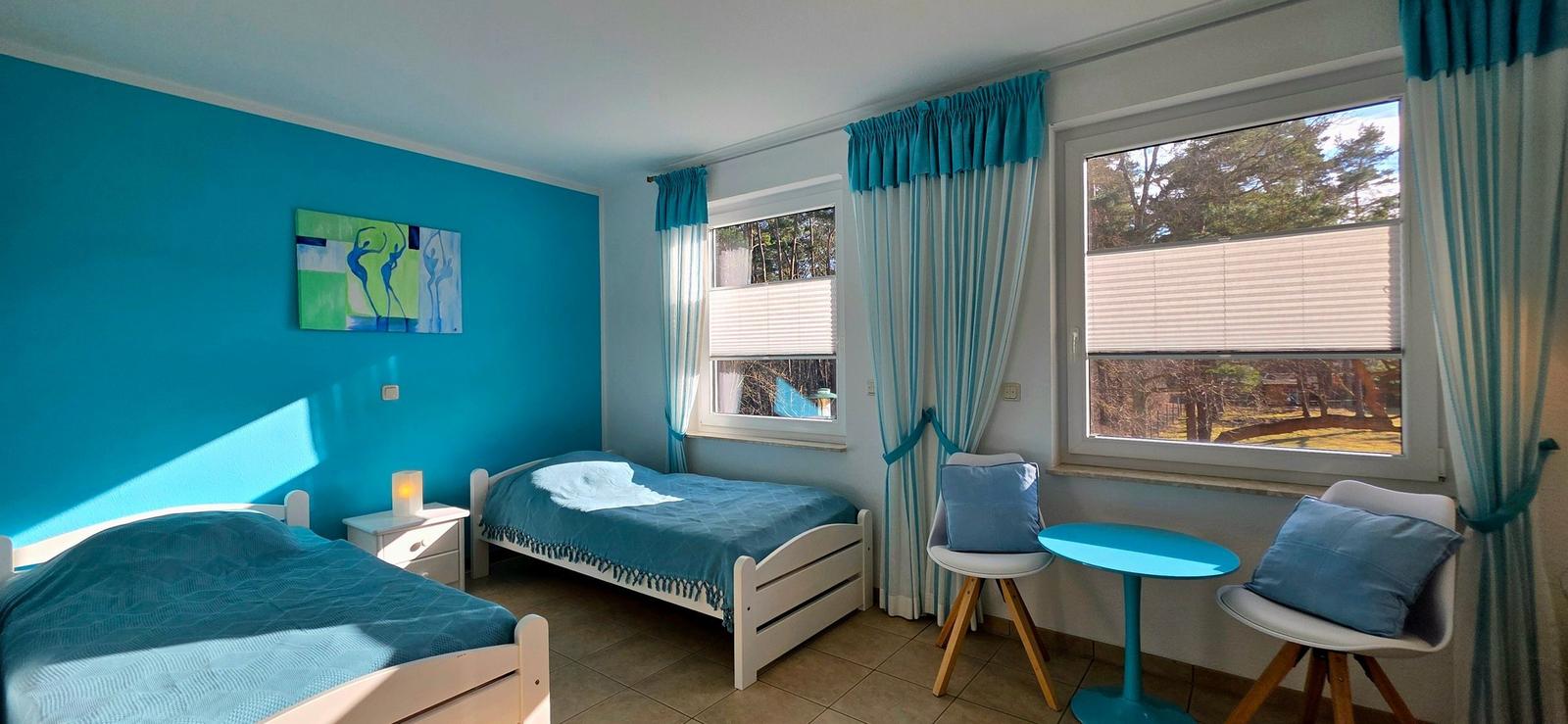 Zwei Betten, Fenster mit Vorhängen und Tisch mit Stühlen im Zimmer.