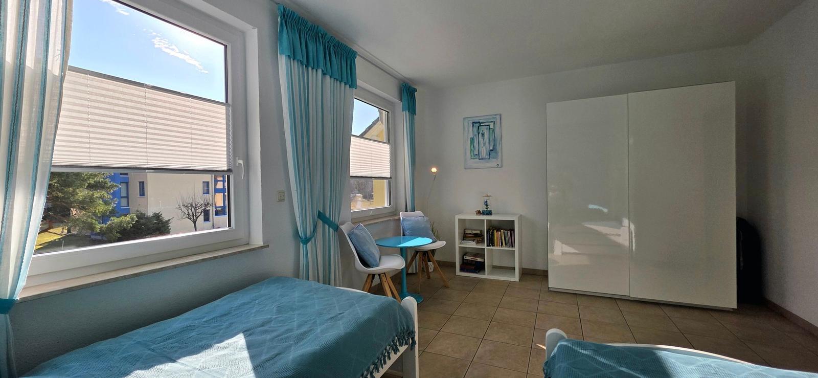 Zimmer mit zwei Betten, Fenstern mit blauen Vorhängen und Schrank.