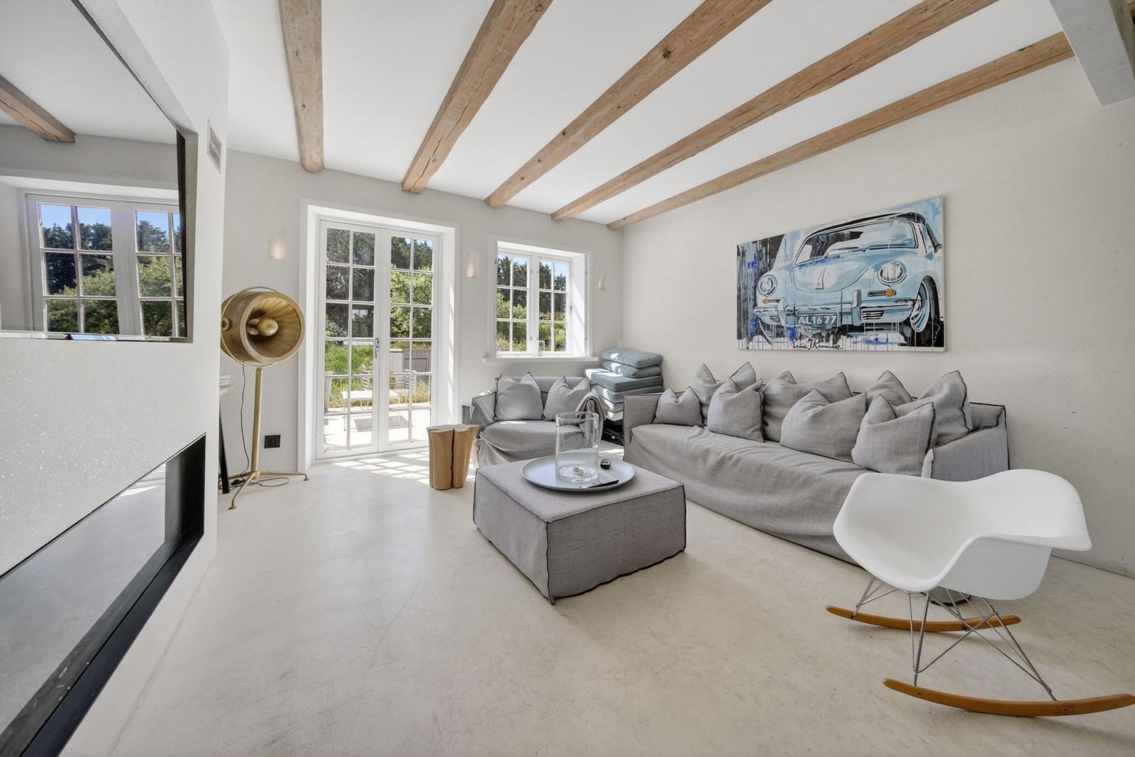 Wohnzimmer mit grauem Sofa, weißer Schaukelstuhl und Holzbalken an der Decke.