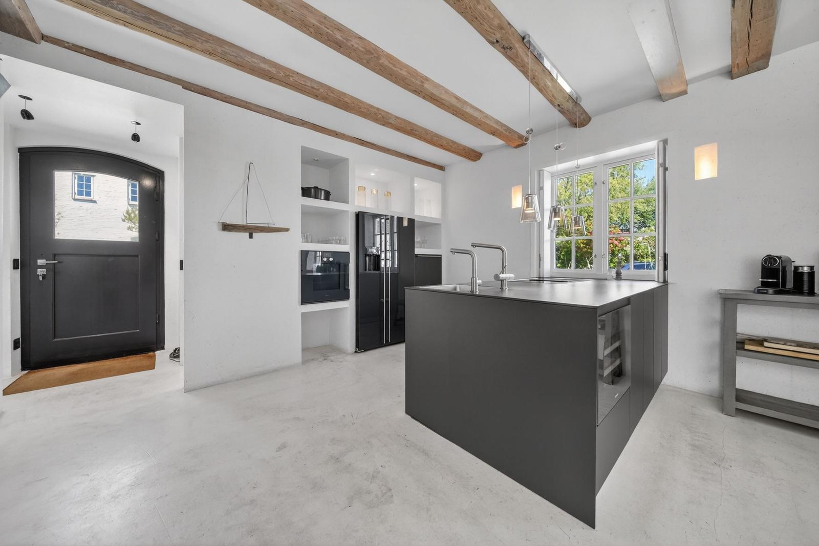 Moderne Küche mit Kücheninsel, Holzbalken und Fenster mit Blick auf Garten.