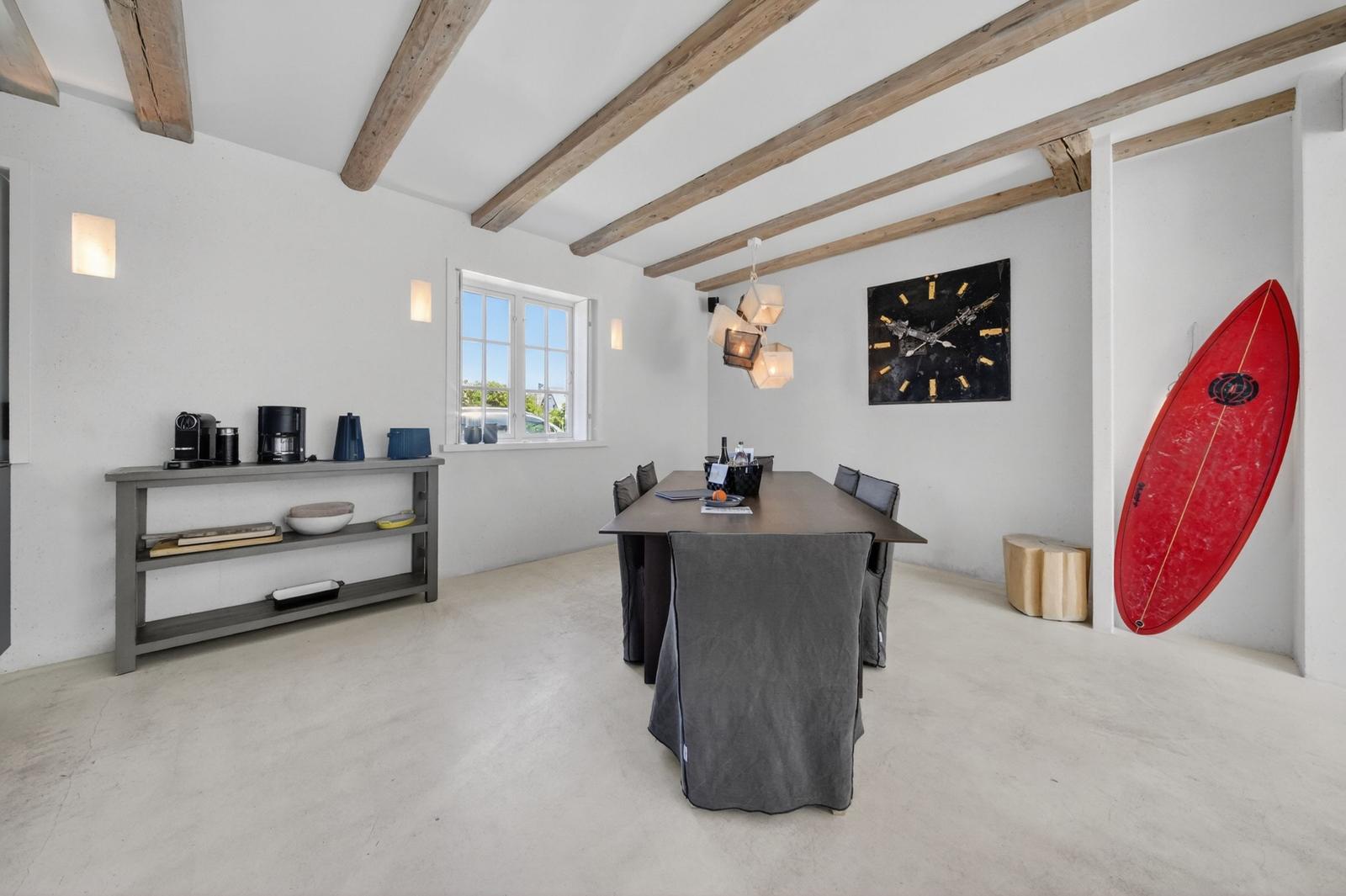 Esszimmer mit Holzbalken, Tisch, Stühlen und rotem Surfbrett an der Wand.