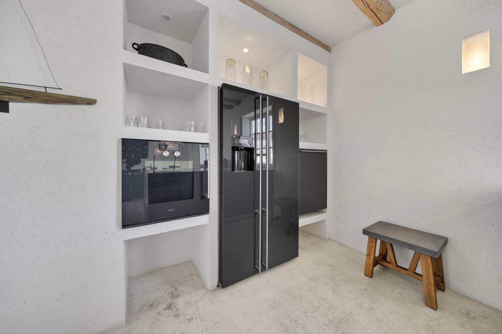 Küche mit schwarzer Kühlschrank und eingebauter Backofen, weiße Wände und Holzbalken.
