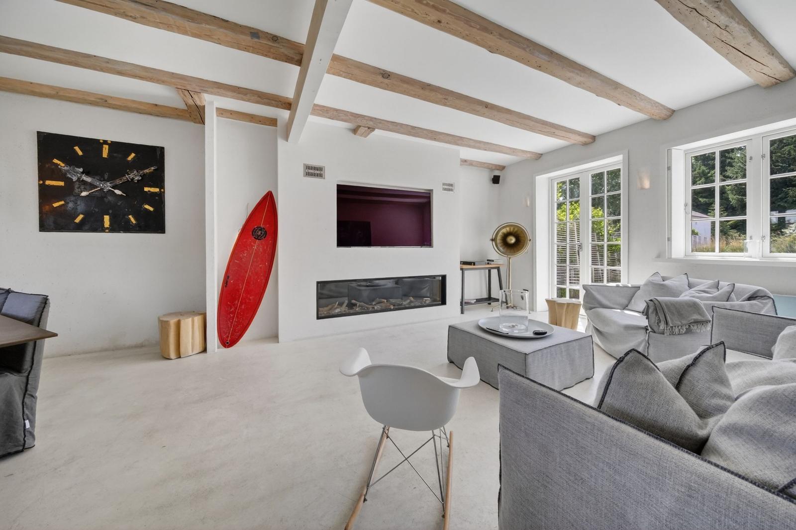 Wohnraum mit Holzbalken, rotem Surfbrett, Sofa und Kamin.