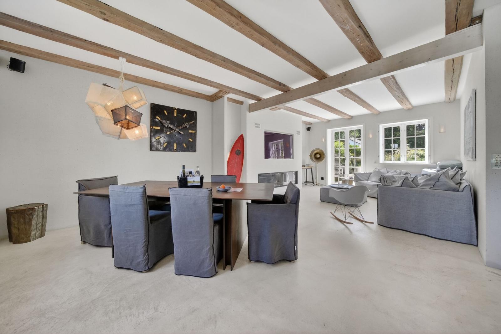Großes Wohn- und Esszimmer mit Holzbalken, grauer Couch und Esstisch mit Stühlen.