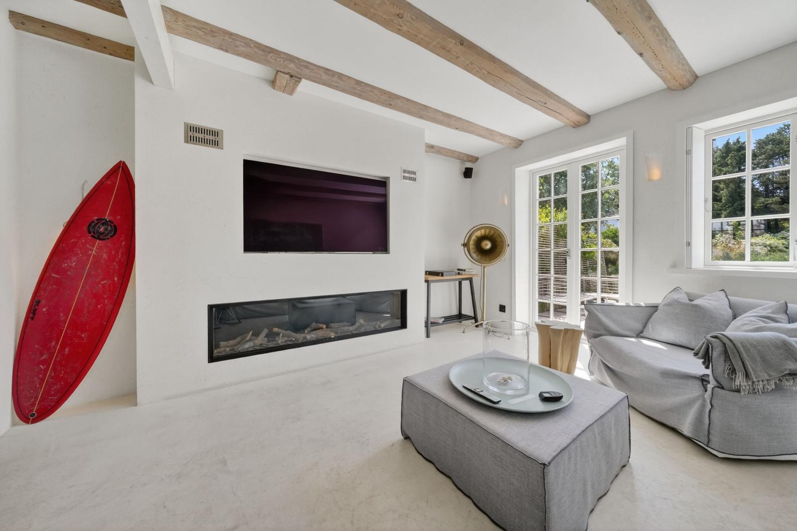 Wohnzimmer mit Kamin, Sofa und rotem Surfbrett an der Wand.