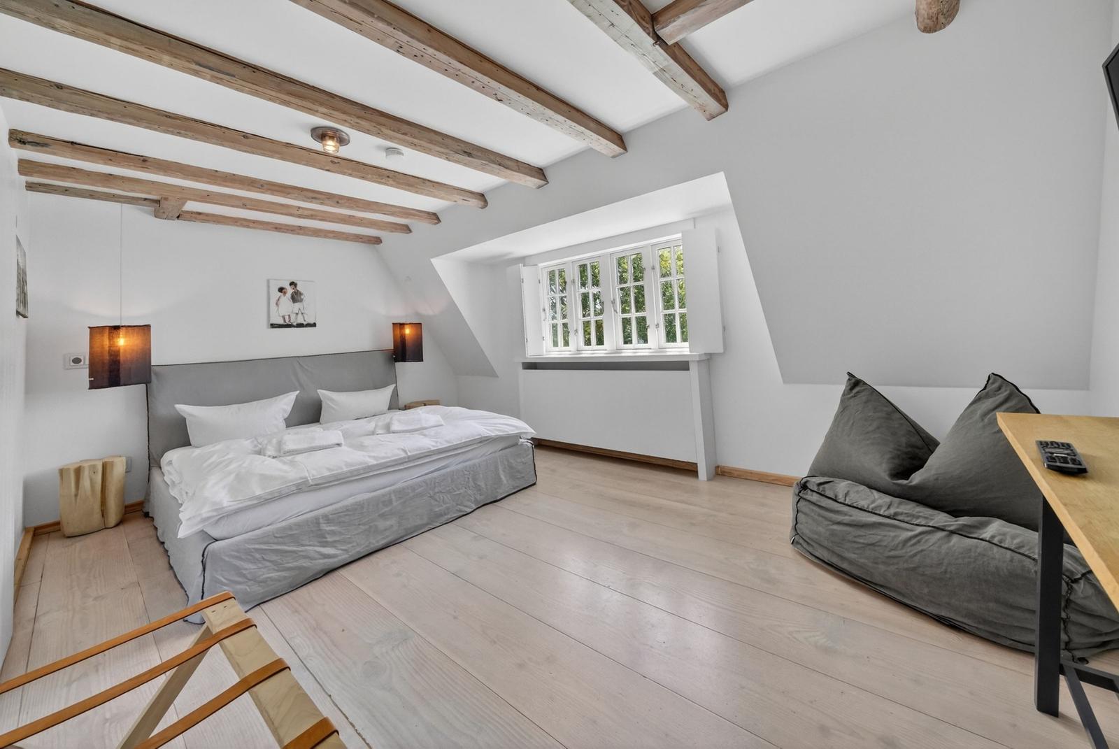 Schlafzimmer mit Dachschrägen, Holzbalken, Bett und Fenster.
