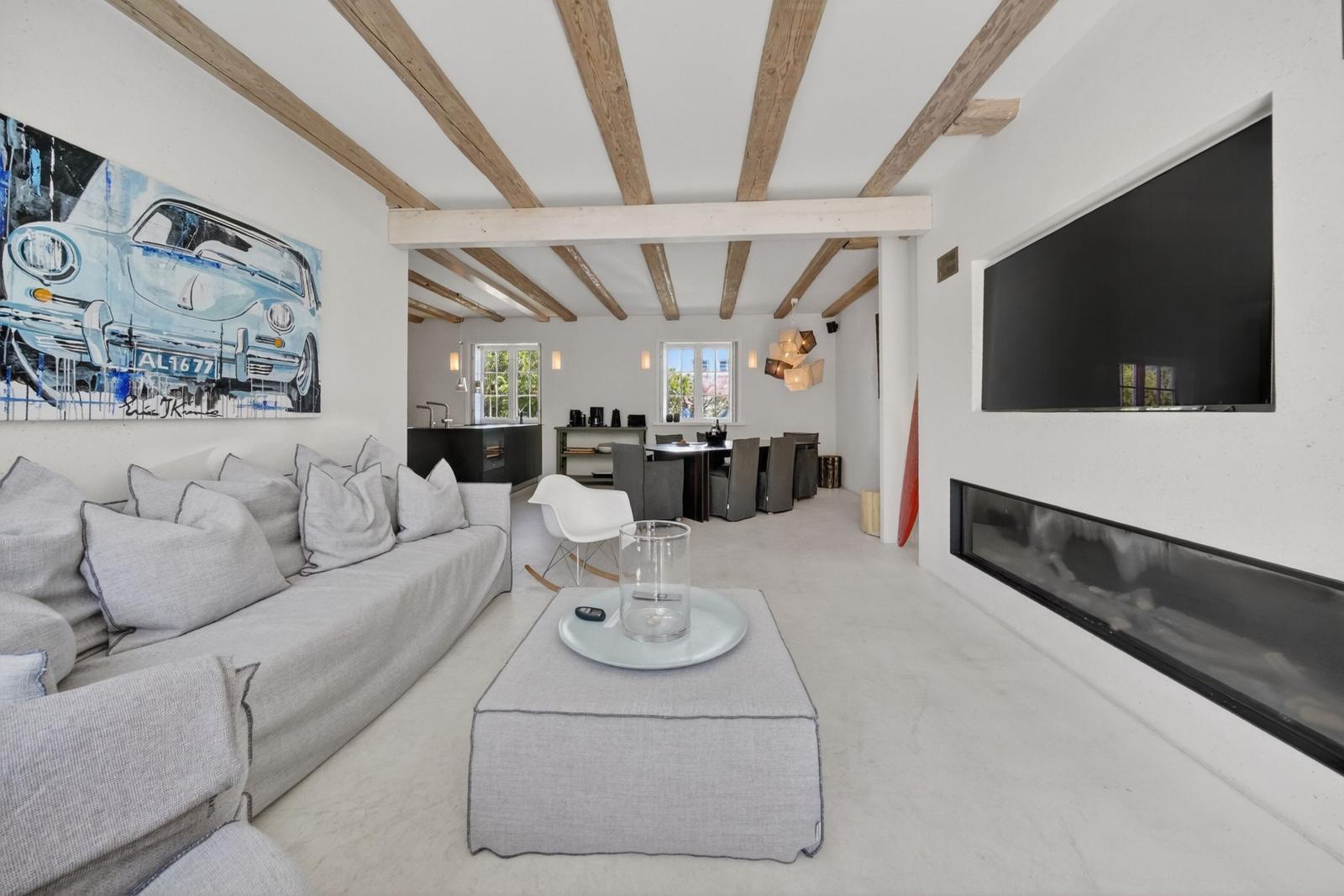 Wohnzimmer mit Sofa, Kamin und Fernseher. Holzbalken an der Decke und Wandbild mit Auto.