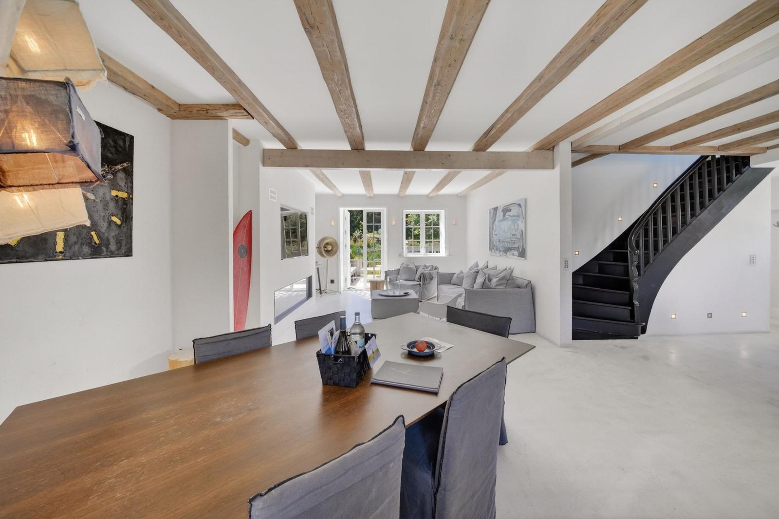 Essbereich mit Tisch und Stühlen, dahinter Wohnbereich mit Sofa und Treppe.