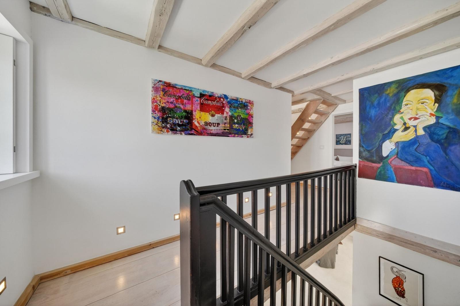 Treppenhaus mit Kunst an den Wänden und Holzbalken an der Decke.