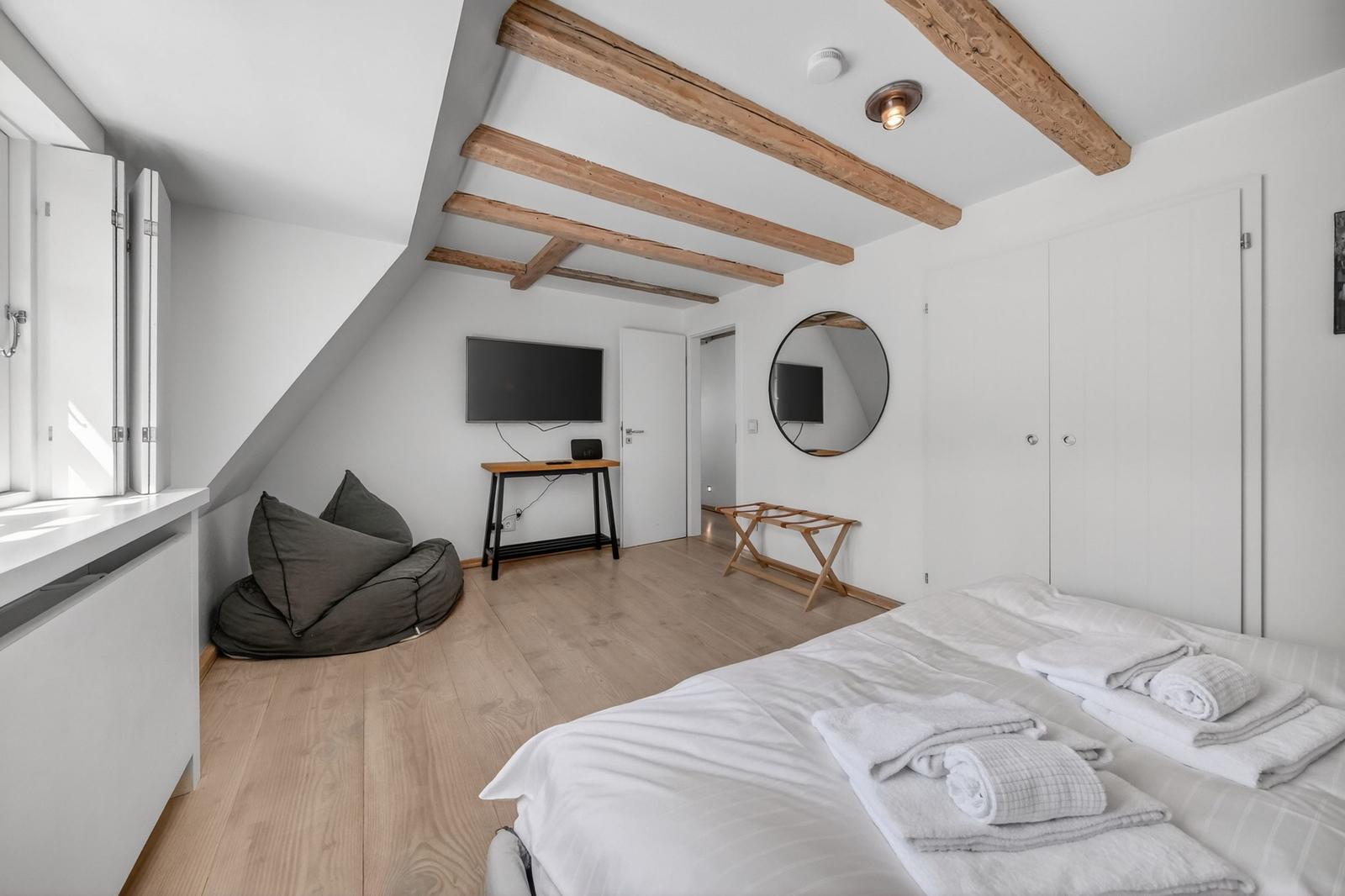 Schlafzimmer mit Bett, Fernseher und Holzbalken an der Decke.
