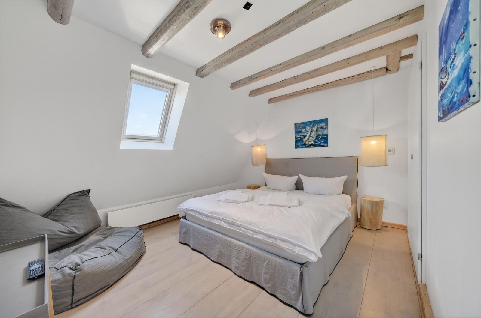 Schlafzimmer mit Doppelbett, Fenster und Holzbalken an der Decke.