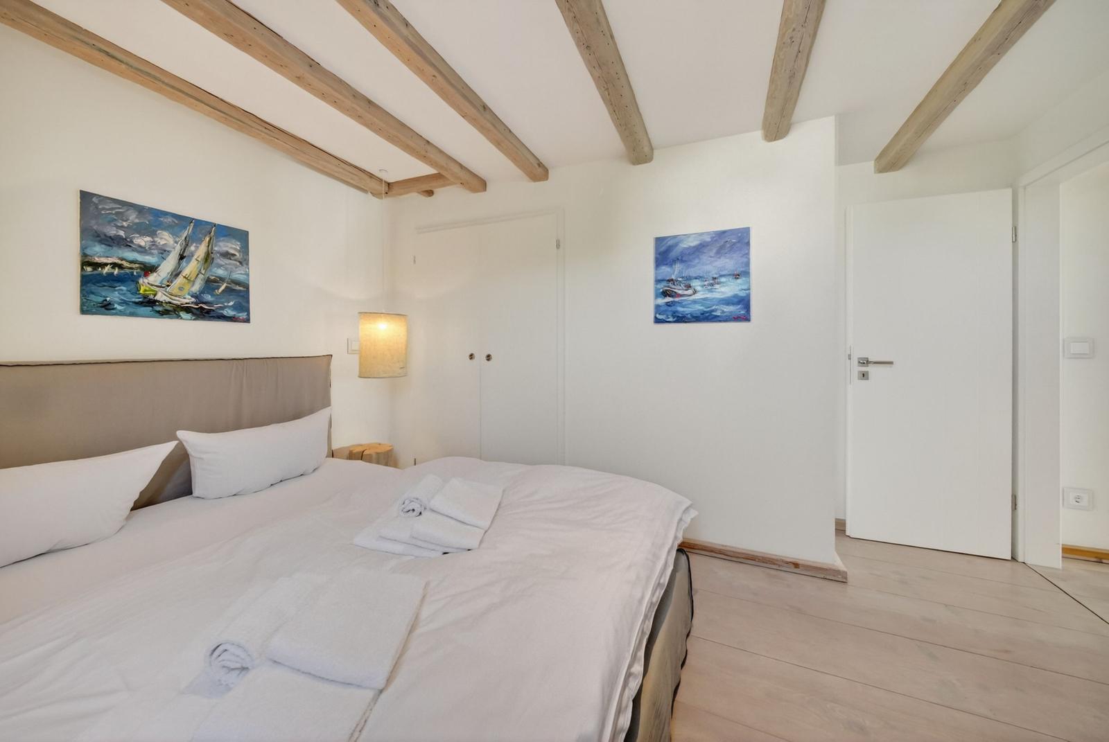 Schlafzimmer mit Bett, Wandbildern und Holzbalken an der Decke.