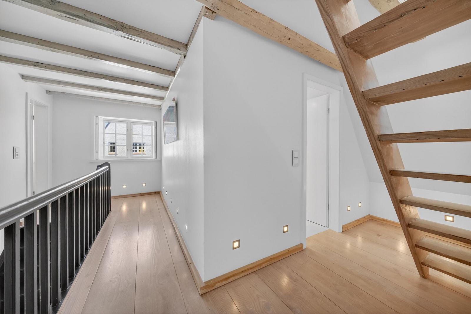 Helle Holzdielen, weiße Wände und Holzstufen in einem Raum mit Dachschrägen und Fenster.