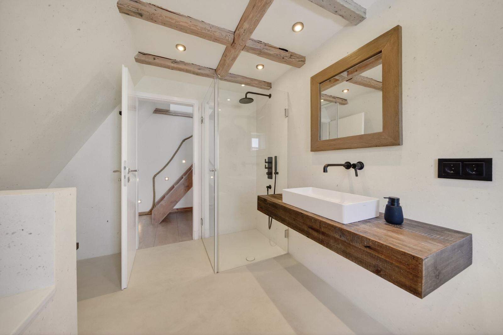 Badezimmer mit Dusche, Waschbecken und Spiegel. Holzbalken an der Decke.