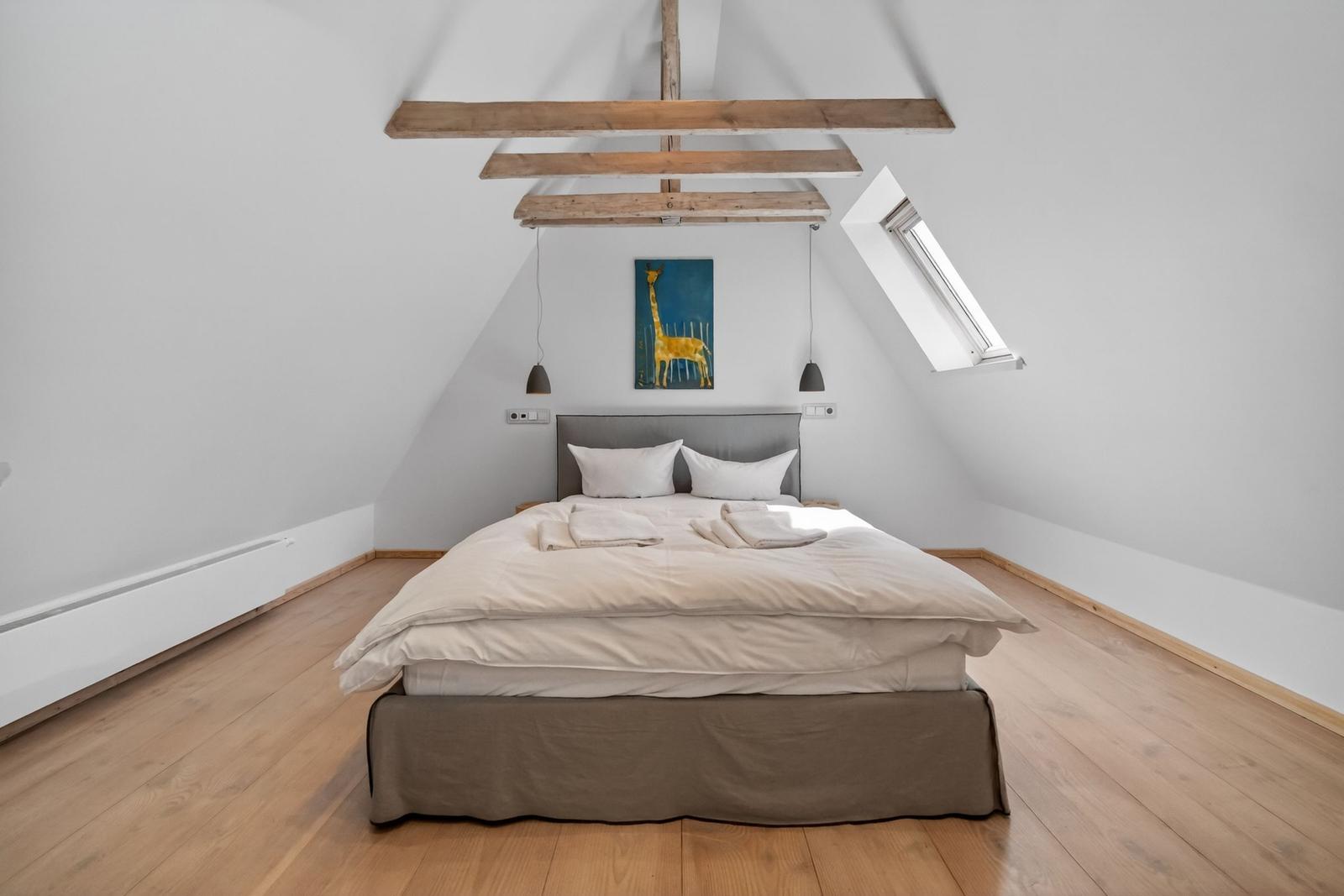 Schlafzimmer mit Dachschräge, Holzbalken, Bett und Fenster.