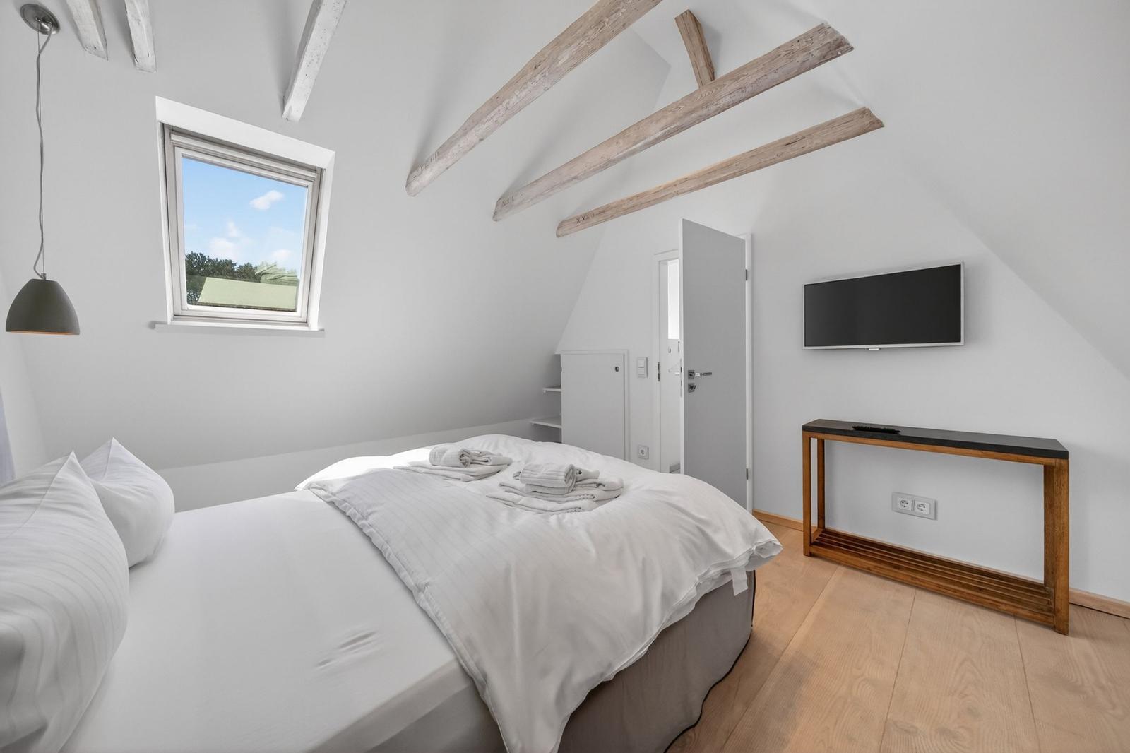 Schlafzimmer mit Dachschrägen, Bett, Fenster und TV.