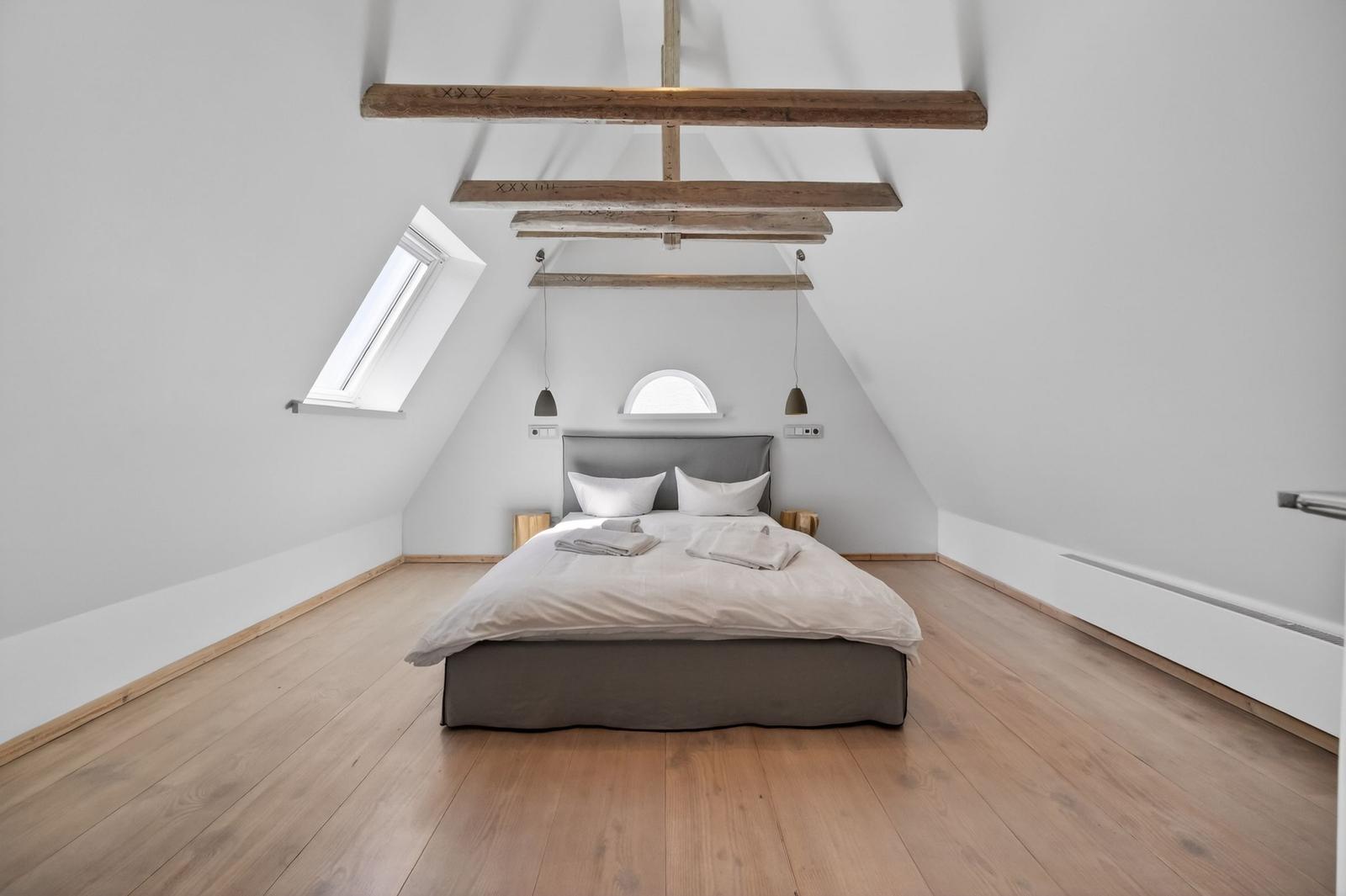 Schlafzimmer mit Dachschrägen, Holzboden und Bett unter Balken.