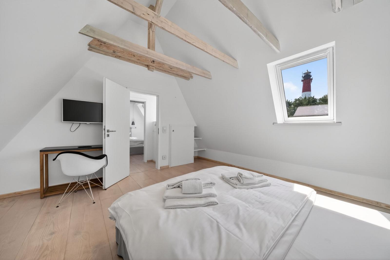 Schlafzimmer mit Blick auf Leuchtturm, Bett, Schreibtisch und Holzbalken.