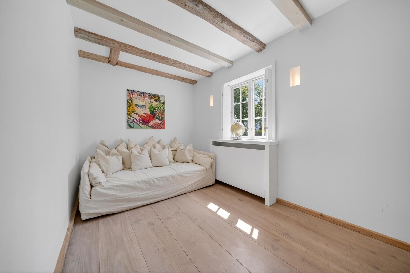 Raum mit Sofa, Fenster und Deckenbalken. Wandbild und Holzboden.