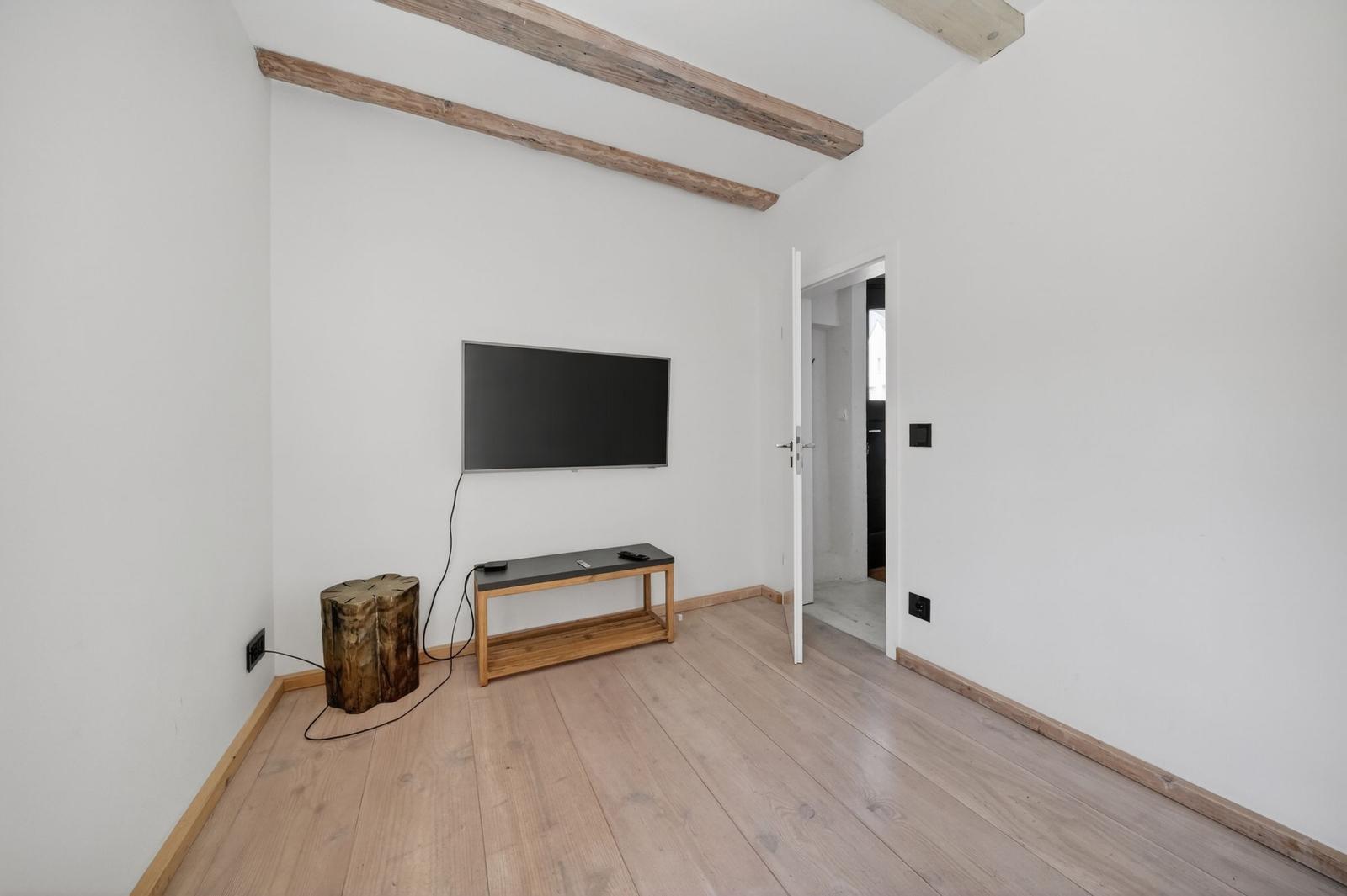 Raum mit Fernseher, Holzfußboden und Balken an der Decke.