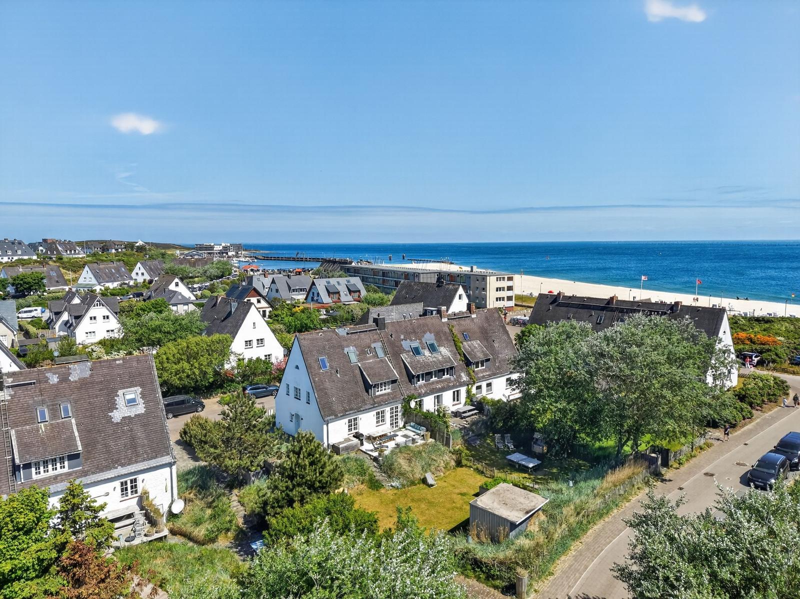 Haus mit Blick auf Strand und Meer. Umgeben von Grün und weiteren Häusern.
