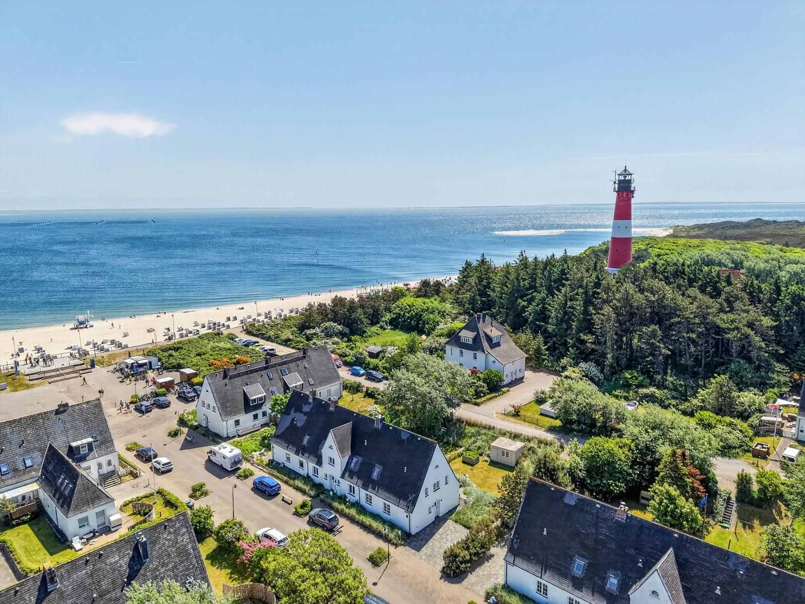 Häuser mit Blick auf Strand und Leuchtturm. Blick auf Küstenlandschaft mit Bäumen und Meer.