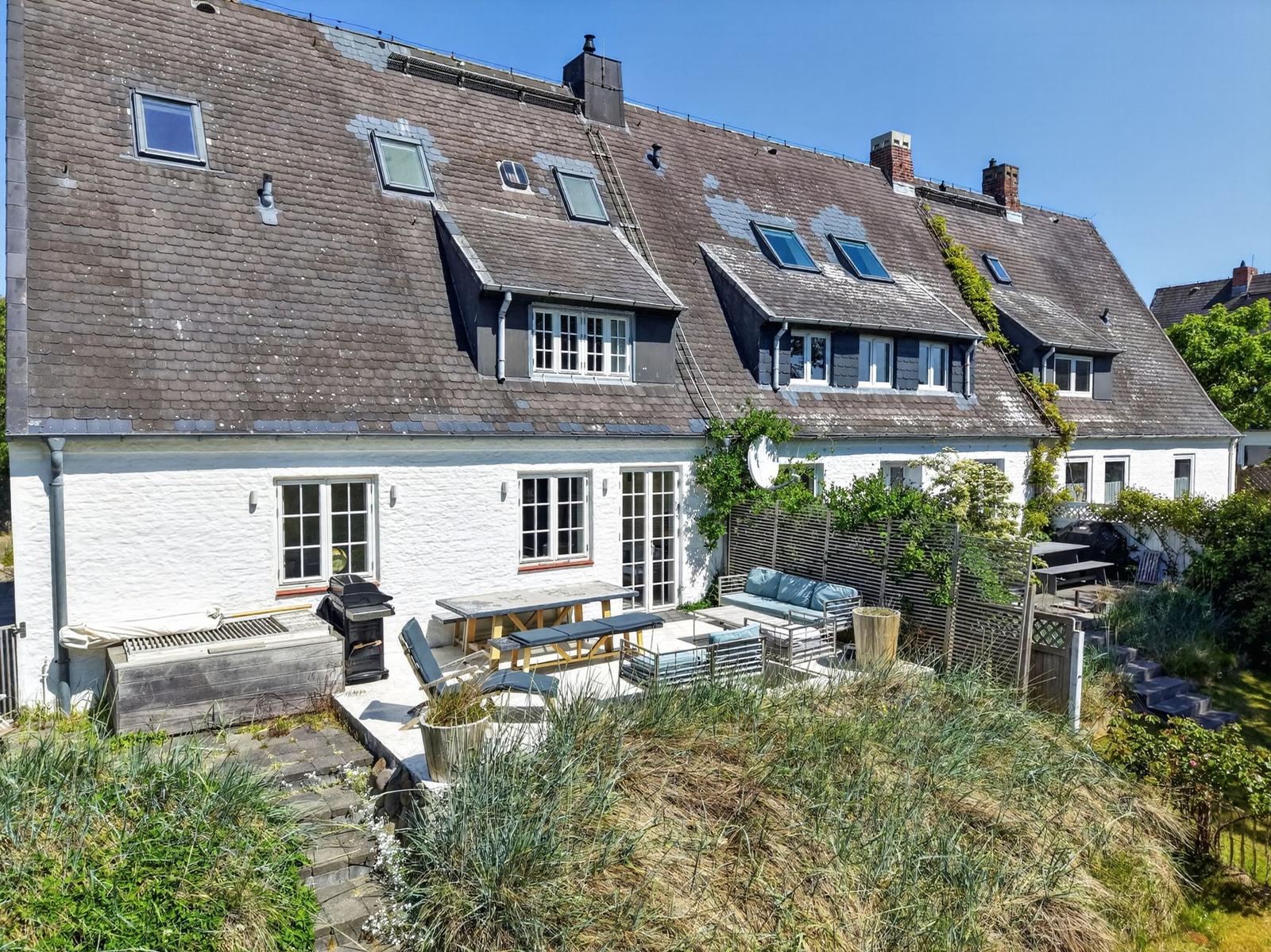 Haus mit Dachgauben, Gartenbereich und Außensitzgelegenheiten.