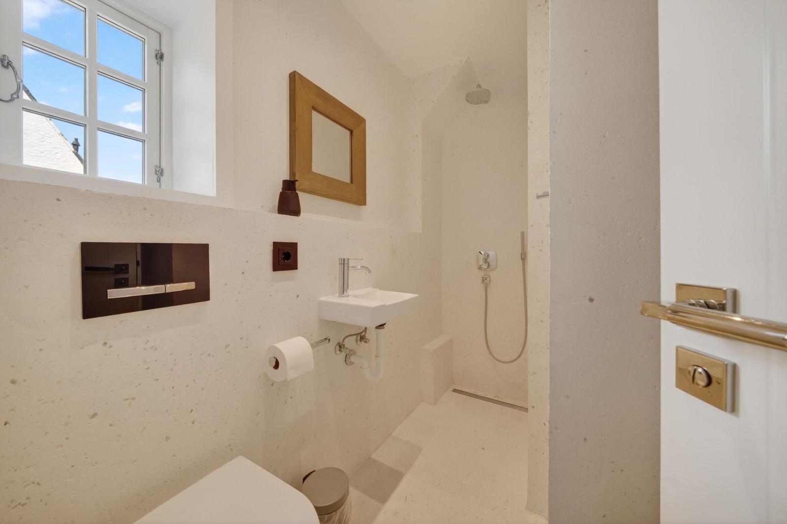 Badezimmer mit Dusche, Waschbecken und Toilette. Fenster mit Blick nach draußen.