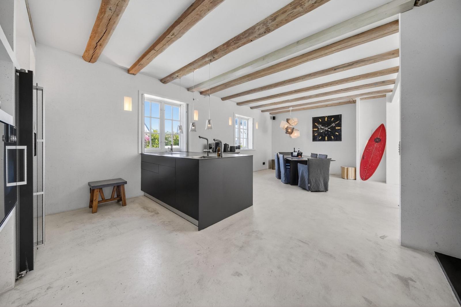 Moderne Küche mit Kücheninsel, Essbereich und roter Surfboard an der Wand.