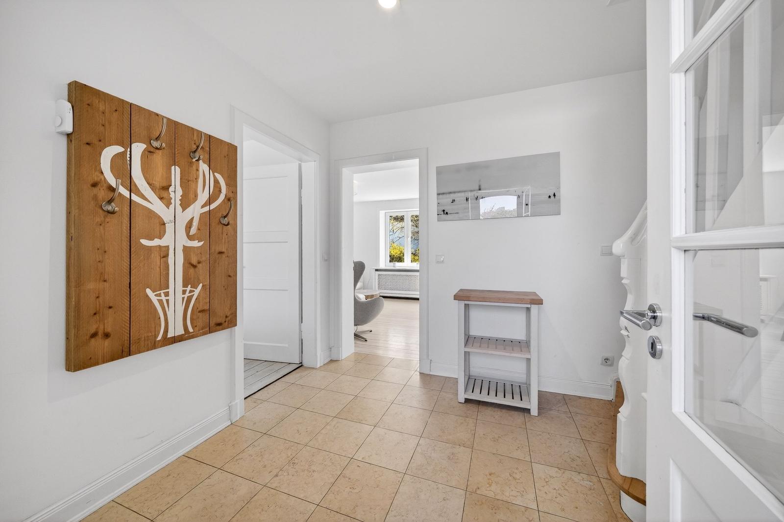 Eingangsbereich mit Holzgarderobe, Tisch und Blick in Wohnzimmer.