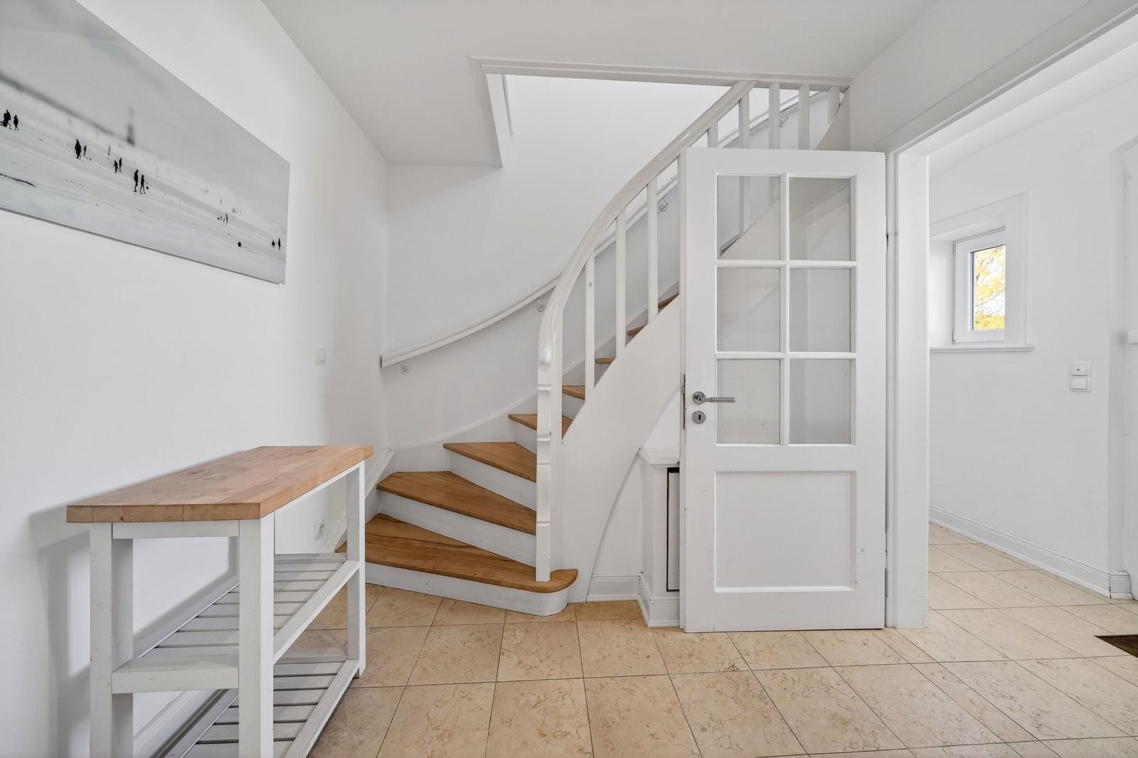 Eingangsbereich mit Holztreppe, weiße Treppe und Tür mit Glasfenstern.