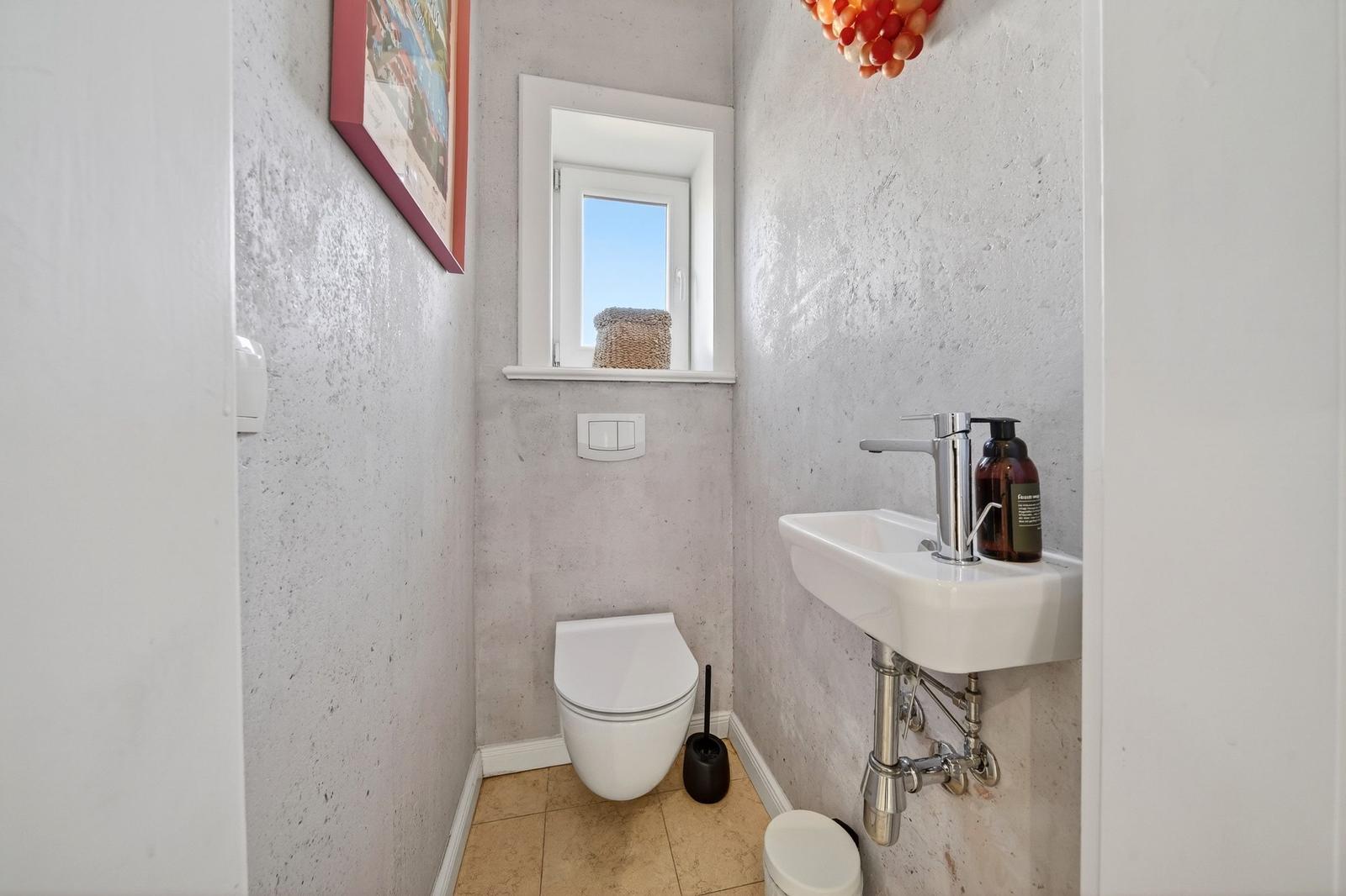 Badezimmer mit Toilette, Waschbecken und Fenster. Wandfarbe hellgrau.