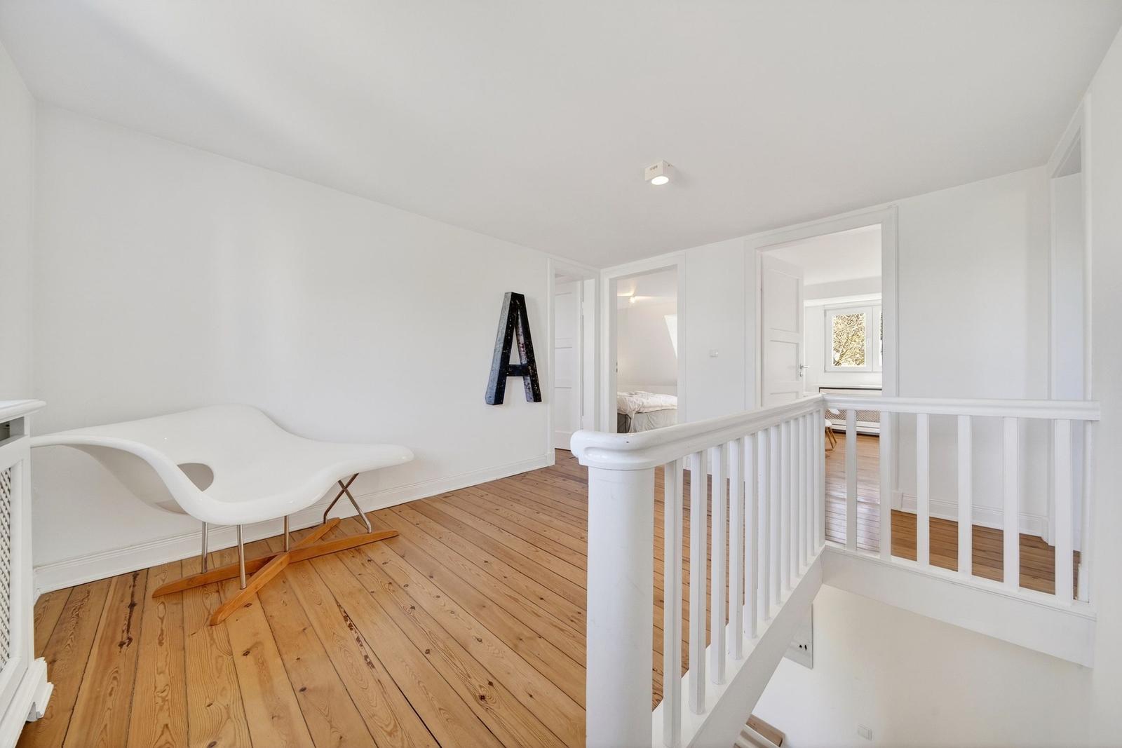 Räumlichkeiten mit Holzboden und weißer Wand. Eine weiße Sitzgelegenheit und ein großes A an der Wand.