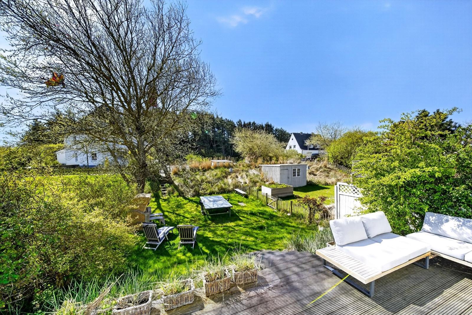Terrasse mit weißen Liegen, grüner Wiese und Blick auf Wald und Himmel.