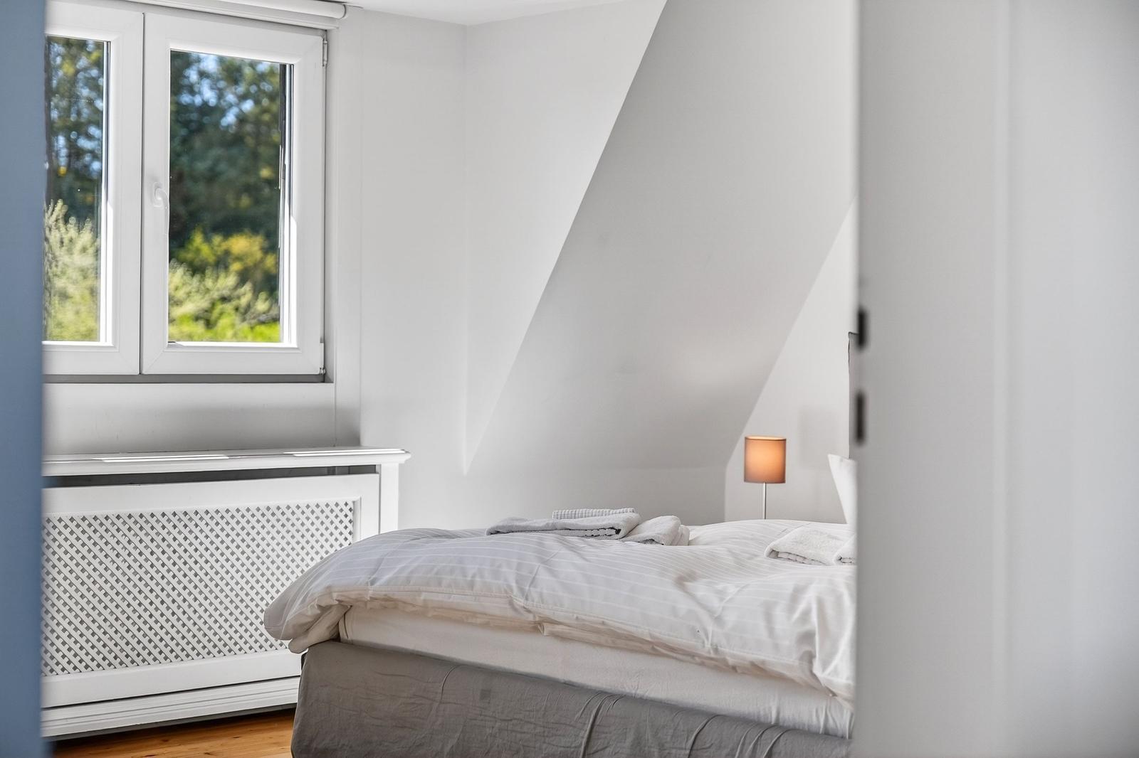 Schlafzimmer mit Dachbodenneigung, Fenster und Bett mit Bettwäsche.