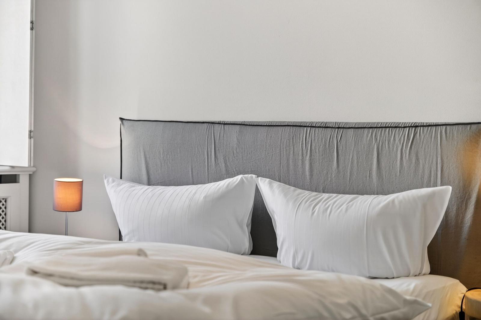 Ein Bett mit weißer Bettwäsche und zwei Kissen vor einem grauen Kopfteil.