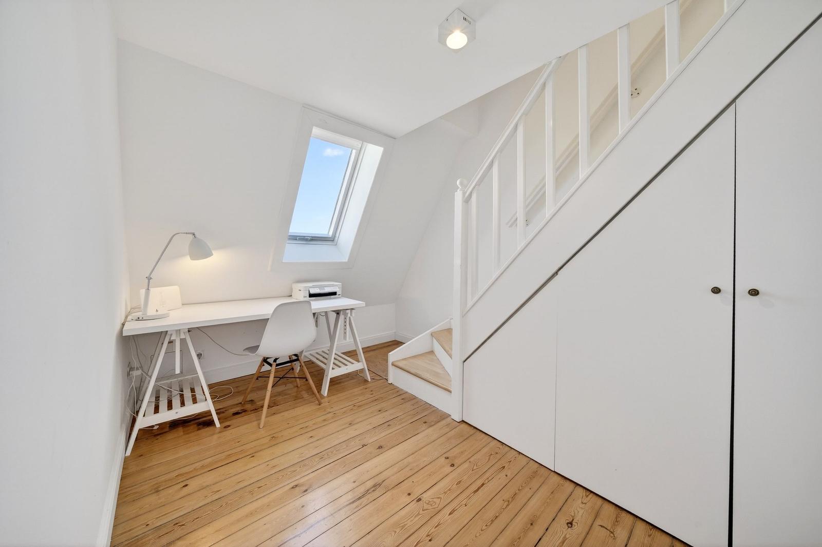 Helle Dachgeschosswohnung mit Schreibtisch, Fenster und Treppe.