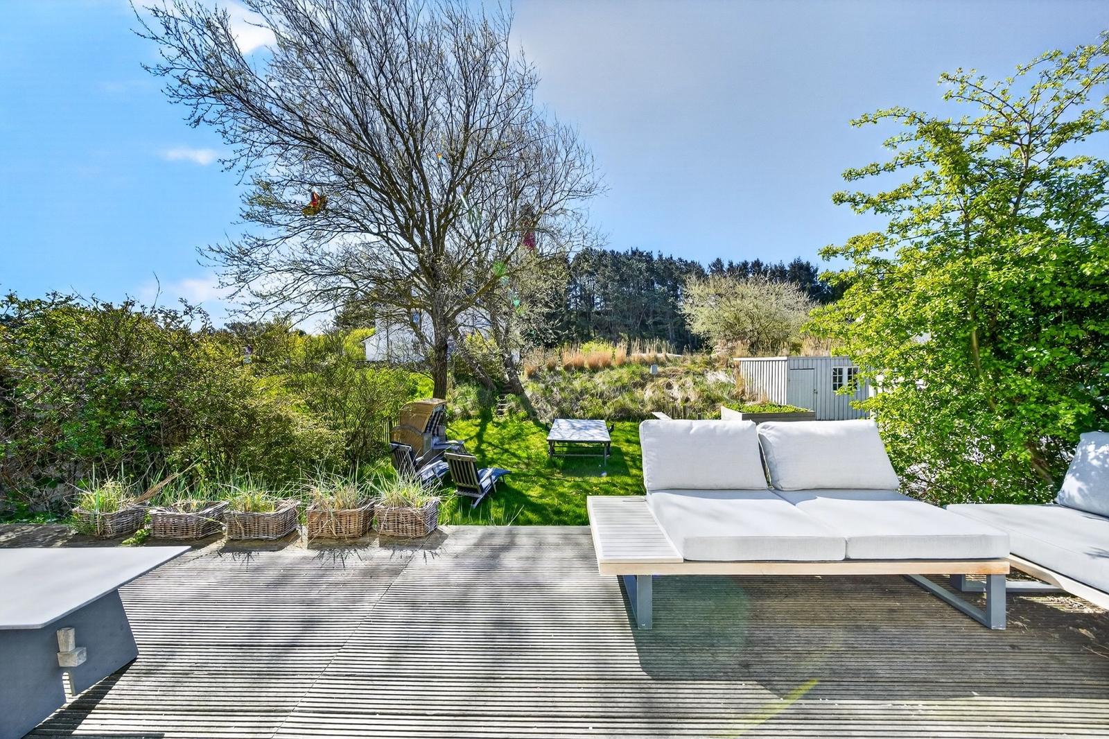 Terrasse mit Liegen und Blick auf grünen Garten mit Bäumen und Himmel.