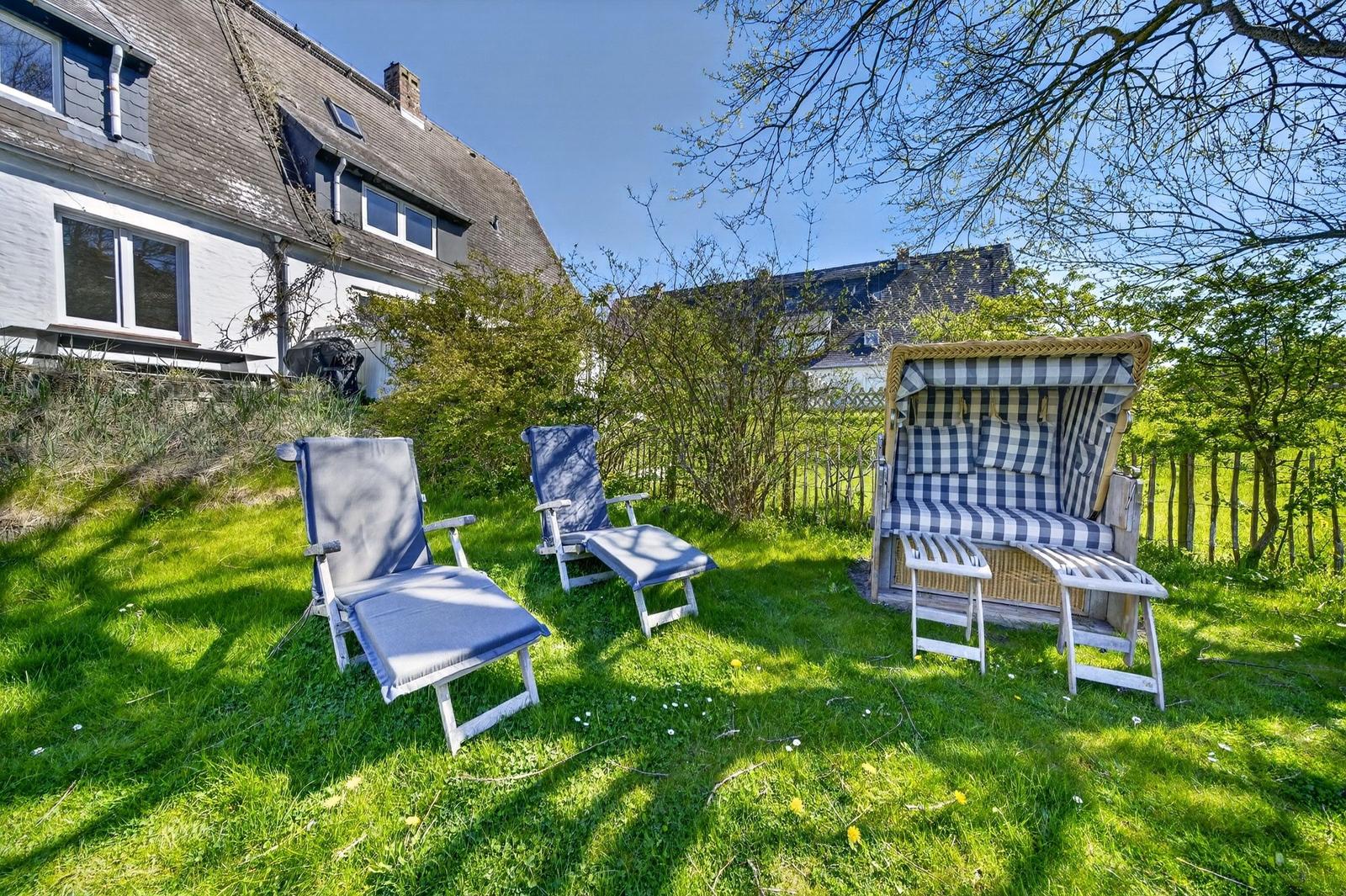 Garten mit Liegestühlen und Strandkorb auf grünem Rasen vor Haus.