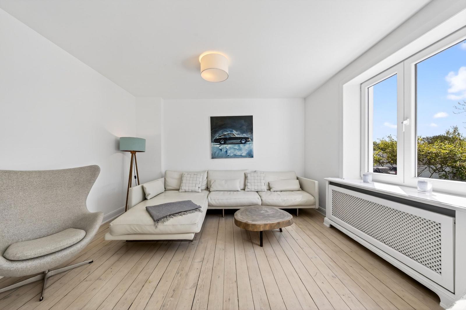 Wohnzimmer mit Sofa, Sessel und Holzboden. Fenster mit Blick auf Grünflächen.