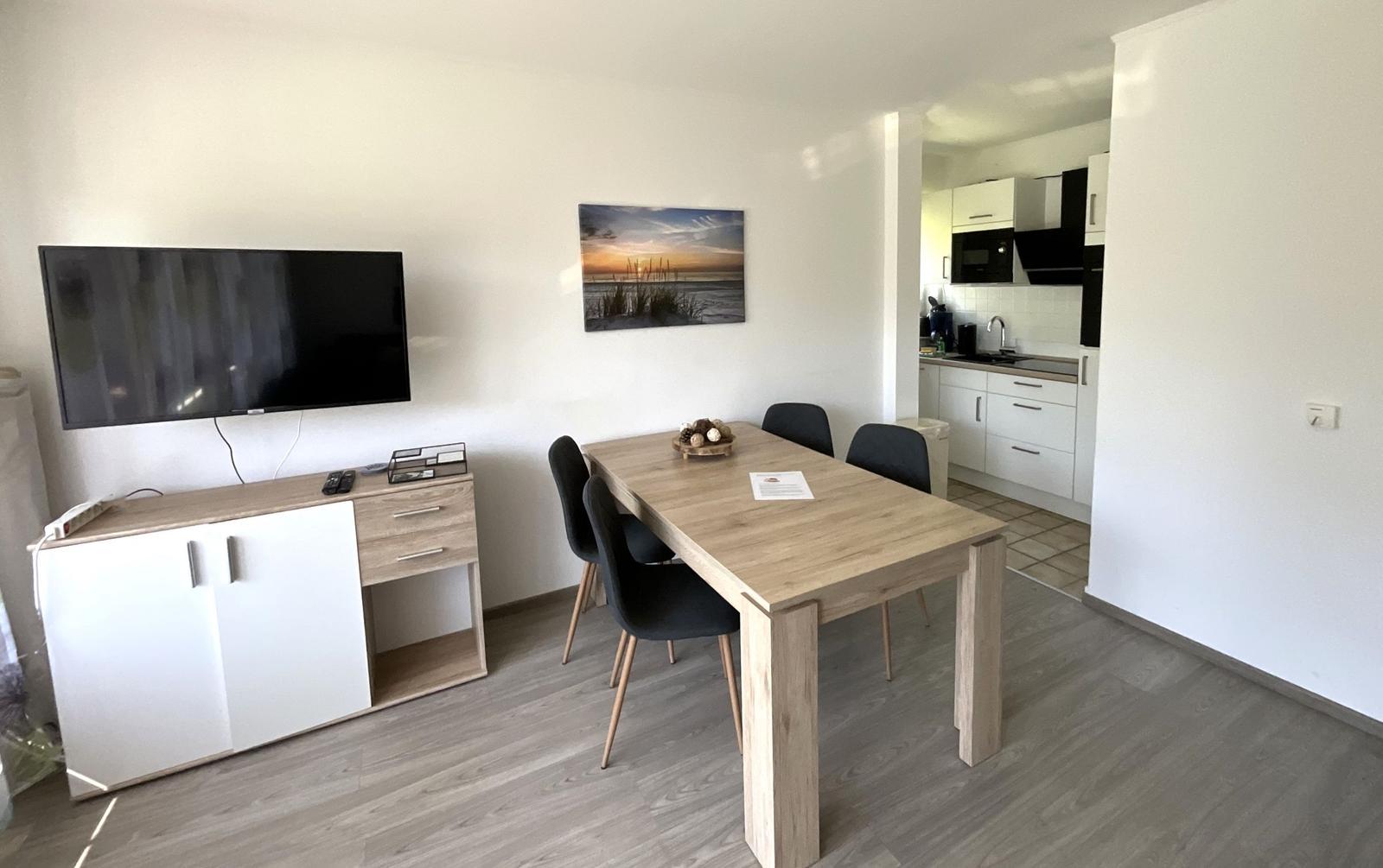 Wohn- und Essbereich mit TV, Esstisch und Küche im Hintergrund.