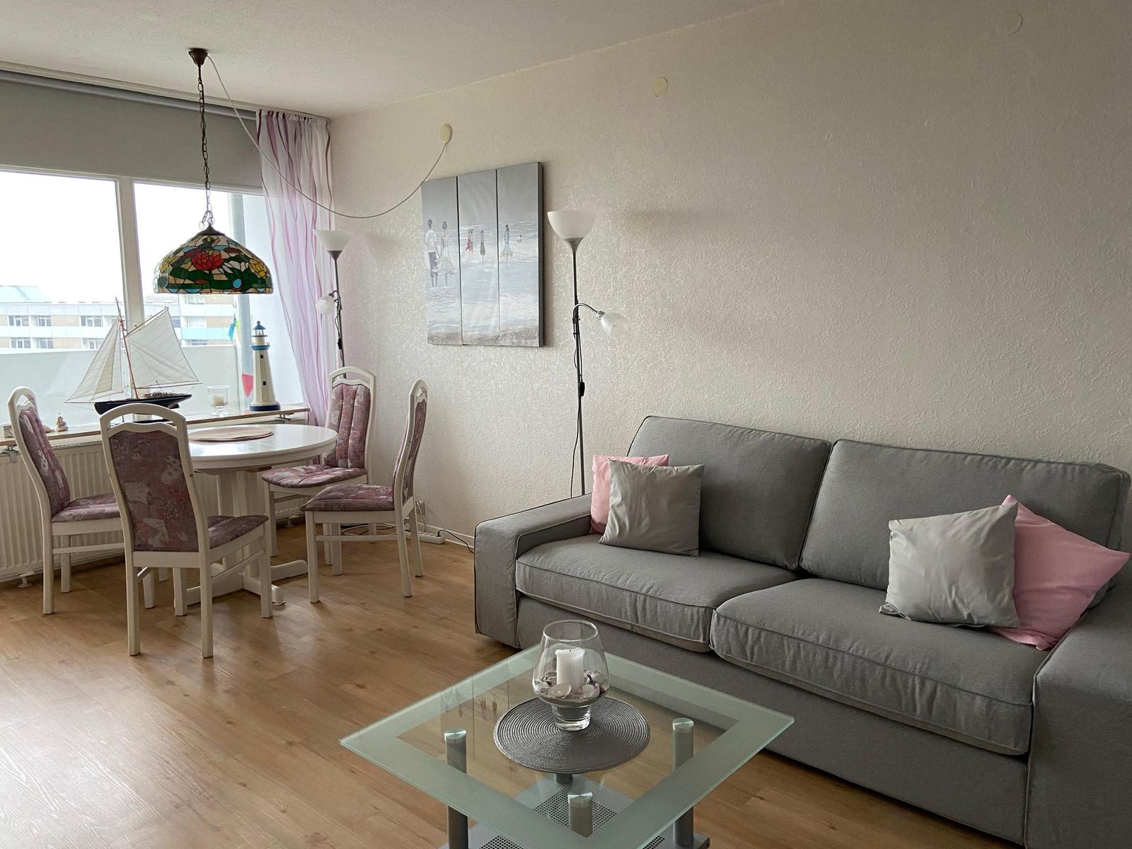 Wohn- und Essbereich mit Sofa, Tisch, Stühlen und Fenster. Dekoration mit Kissen und Lampen.