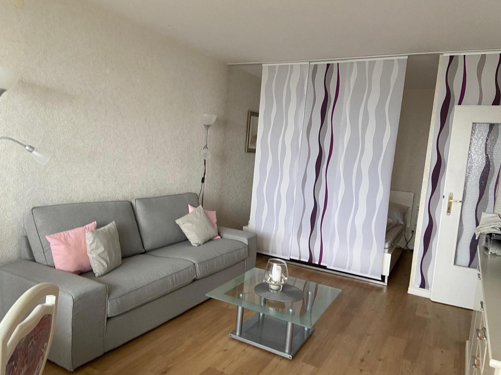 Wohnzimmer mit Sofa, Glas-Tisch und Raumteiler mit Wellenmuster.