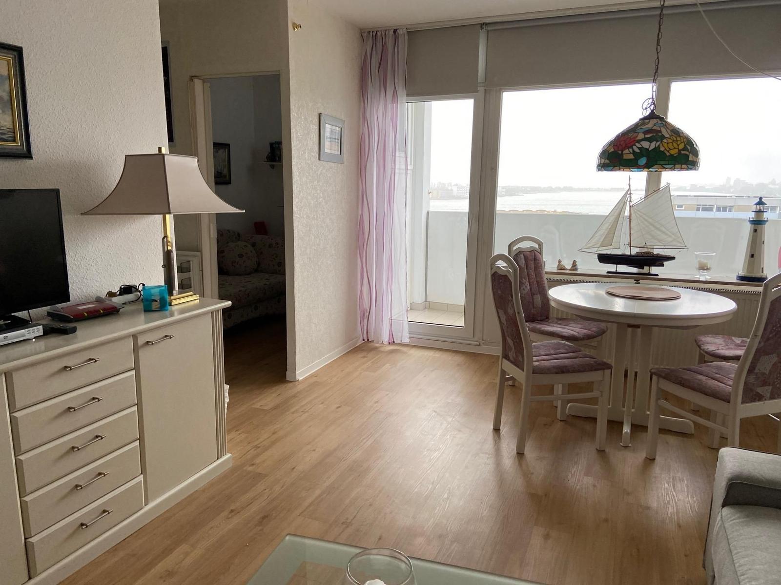 Wohnzimmer mit Essbereich, Balkon und Fernseher. Tisch mit Stühlen und Lampe.