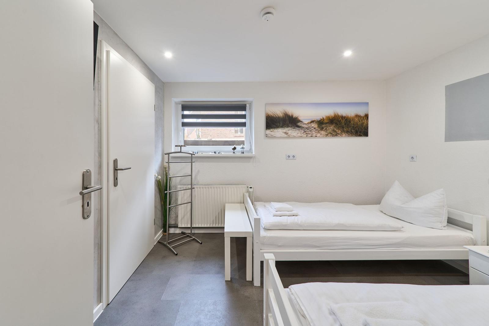 Zimmer mit zwei Betten, Fenster, Heizung und Wandbild.