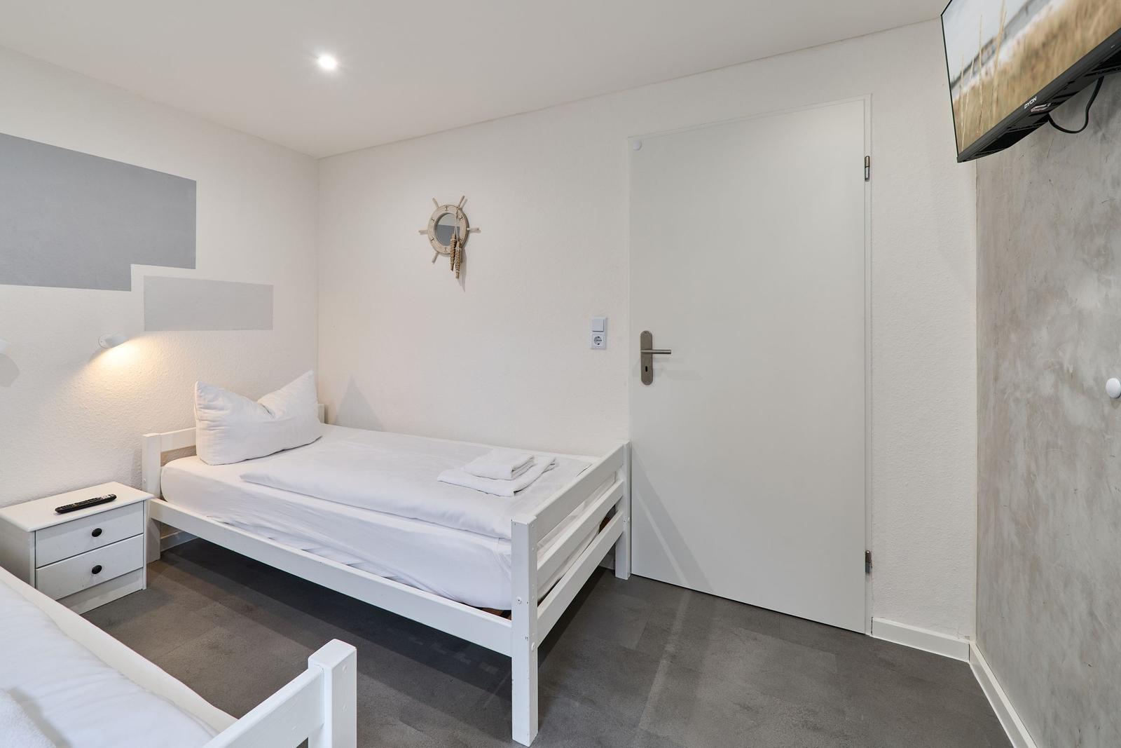 Schlafzimmer mit weißem Bett, Nachttisch und Fernseher an der Wand.