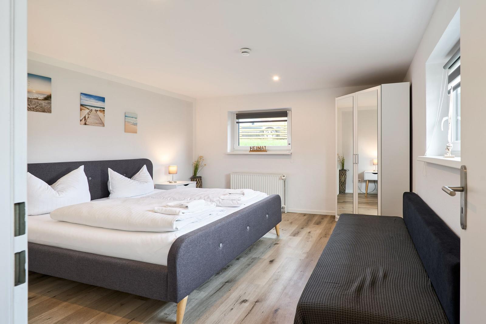 Schlafzimmer mit Bett, Schrank und Fenster. Holzboden und Wandbilder.