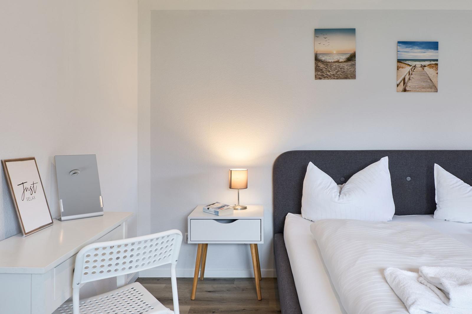 Schlafzimmer mit Bett, Nachttisch und Schreibtisch. Wandbilder zeigen Strand.