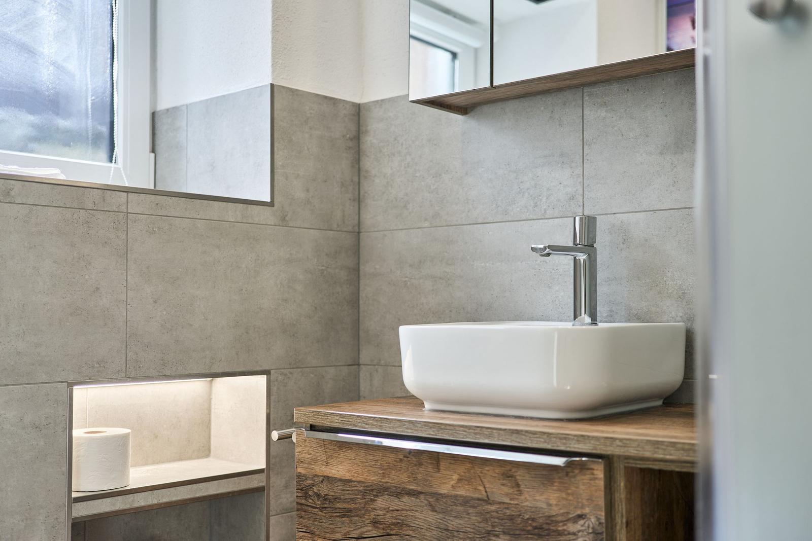 Badezimmer mit Waschbecken, Spiegelschrank und Toilettenpapierablage.