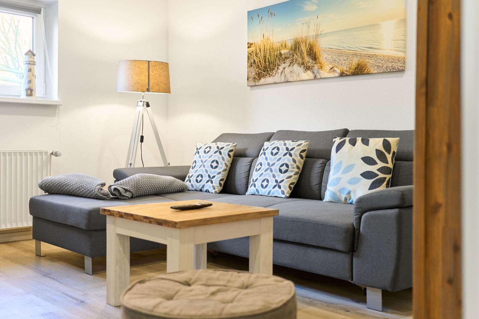 Ein Wohnzimmer mit grauem Sofa, Holztisch und Strandbild an der Wand.